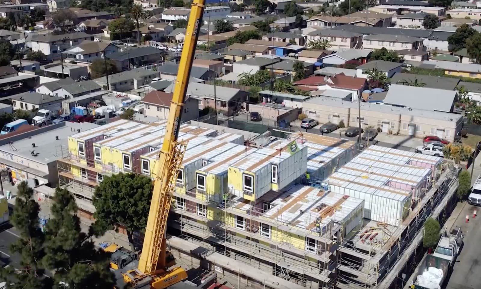 A volumetric steel module being set by crane on a larger multifamily construction site